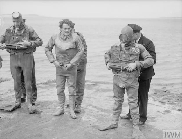 Men of the LCOCU changing into their shallow water diving suits before going in to clear explosives from a beach obstruction. © IWM A 28996 